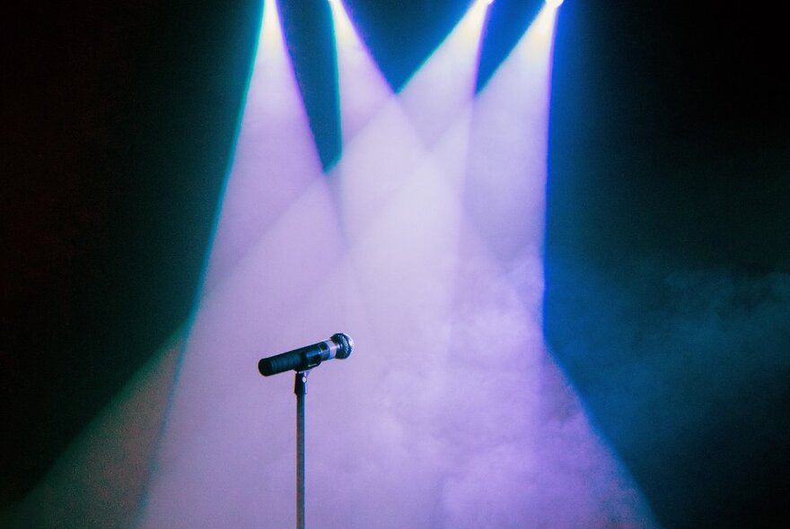 A microphone on stage with four spotlights cast down on it and nobody there. 