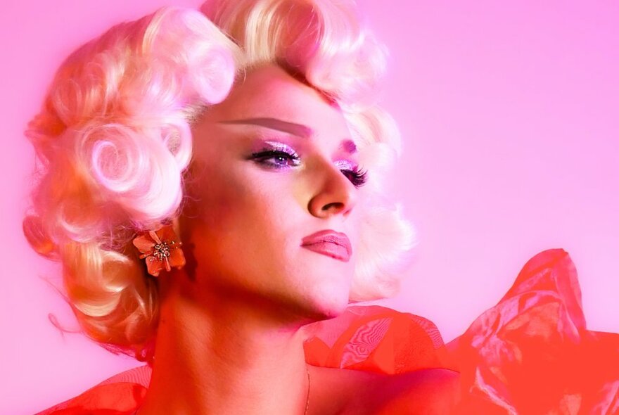Drag artist wearing a blonde 1950s wig, earrings and dramatic makeup.