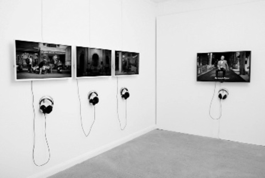 A white room with four large screens hanging from the wall, each displaying a different image, with headphones attached to each monitor.