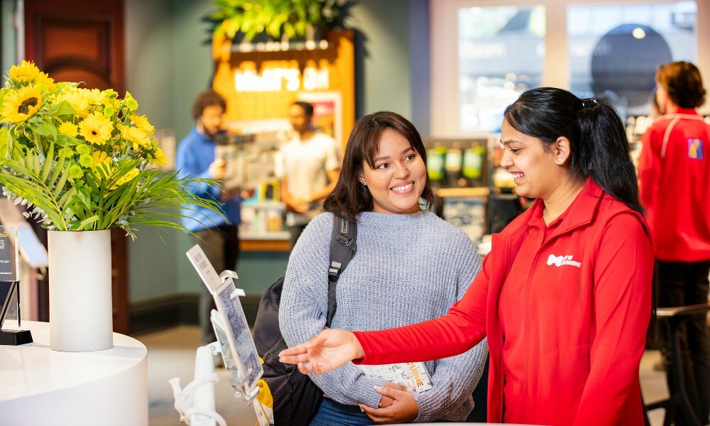 A staff member in a red jacket showing a customer something on a screen.