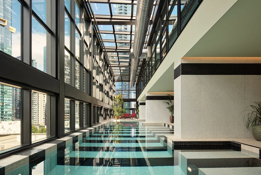 An indoor swimming pool with black and white striped tiling and floor-to-ceiling windows.