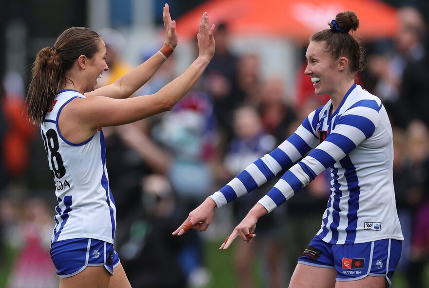 Two North Melbourne AFLW players celebrating on the football field.