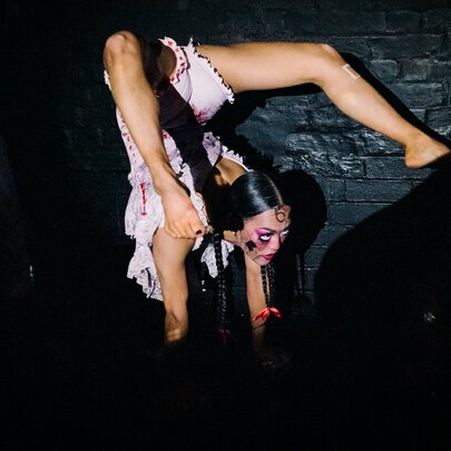 A burlesque dancer doing a handstand with her legs over the back of her head. 