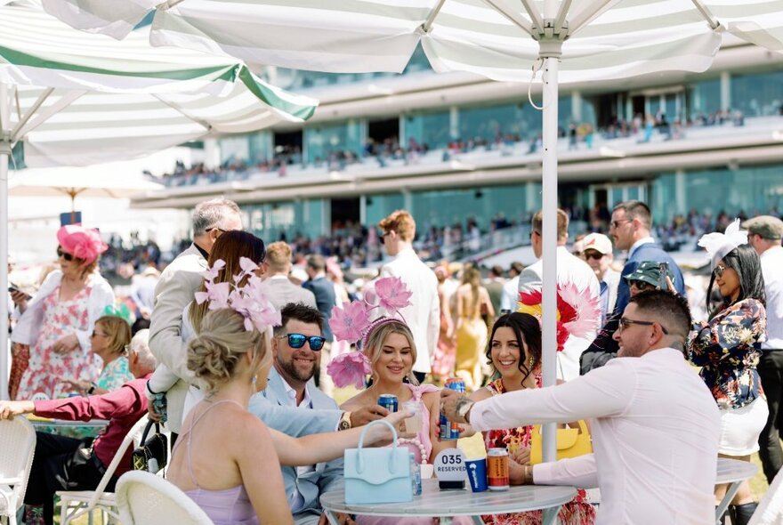 Well-dressed people sitting at tables under umbrellas enjoying themselves. 