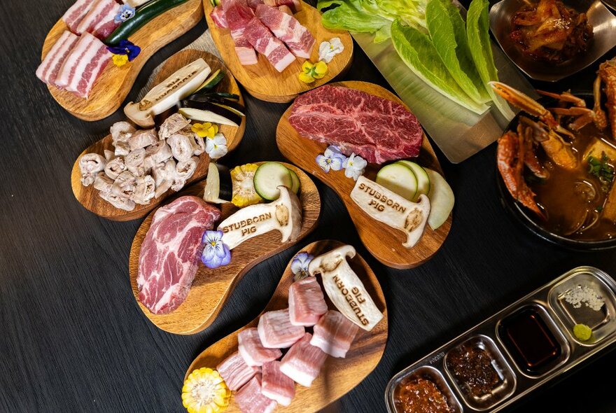 Looking down on a table with small plates of various raw pork cuts and condiments. 