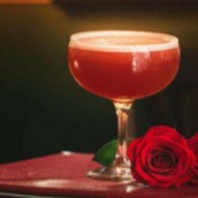 A red cocktail in a martini glass, and two red rosebuds on a table.