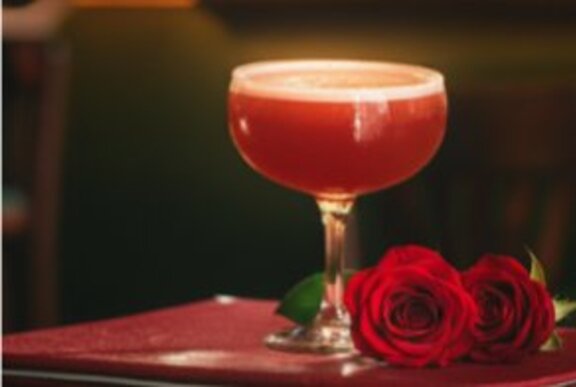 A red cocktail in a martini glass, and two red rosebuds on a table.