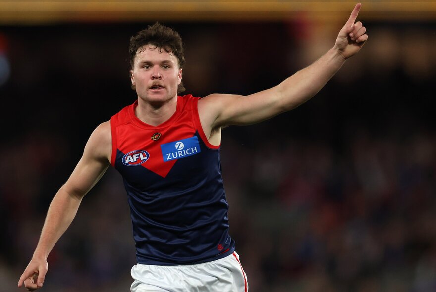 A Melbourne AFL football player with his arm raised above him triumphantly during a match.