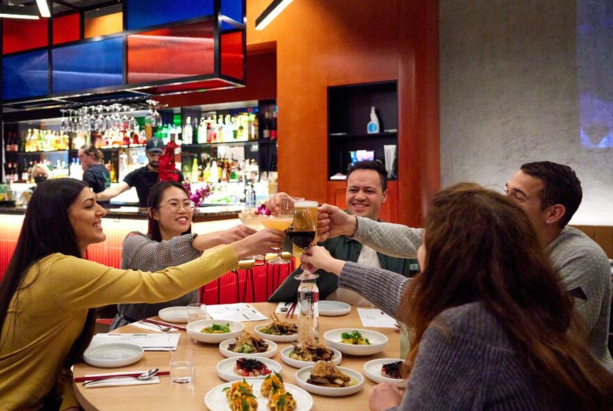 A group of friends are doing a cheers at a restaurant