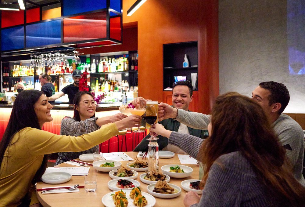 A group of friends are doing a cheers at a restaurant