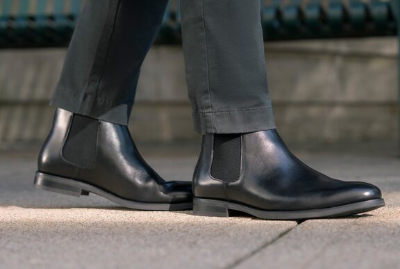 Black leather boots on a person wearing trousers, walking on a footpath.