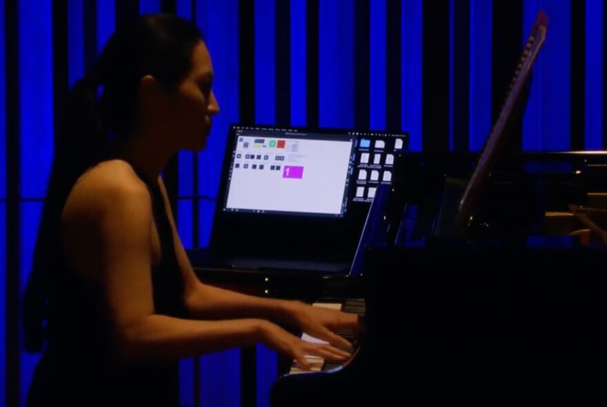 A musician wearing headphones playing a piano with a laptop next to her.