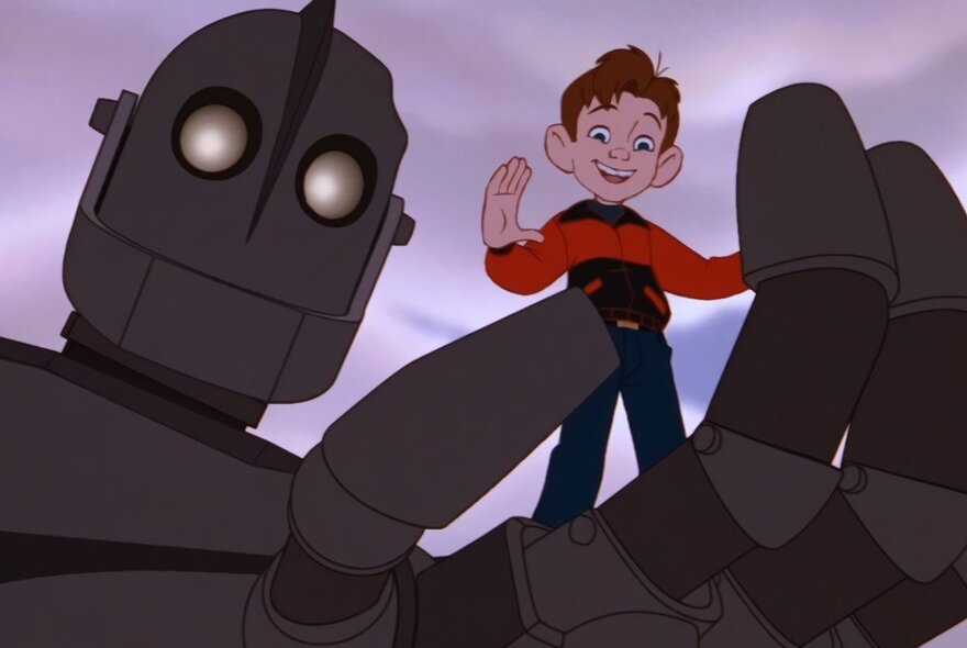 A still from the animated movie, The Iron Giant, of a giant iron robot holding a young boy with red hair in its hand.