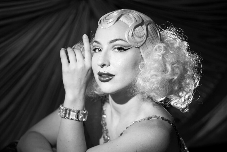 Burlesque performer wearing a curly blonde wig, showgirl makeup and glass bracelet. 