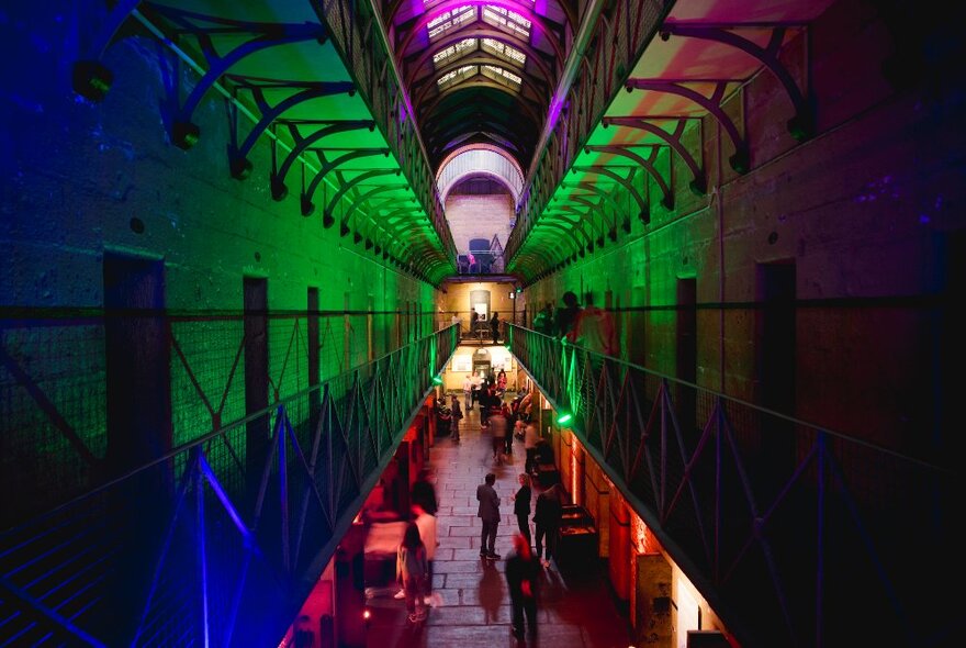 The interior of the Old Melbourne Gaol dimly lit in green, red and blue. 