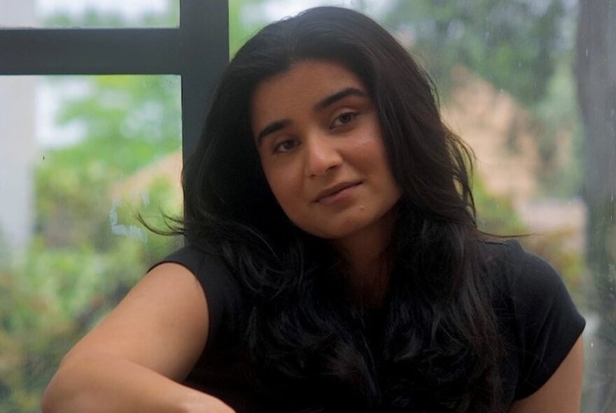 Indian woman with long dark hair, resting one arm on her leg.