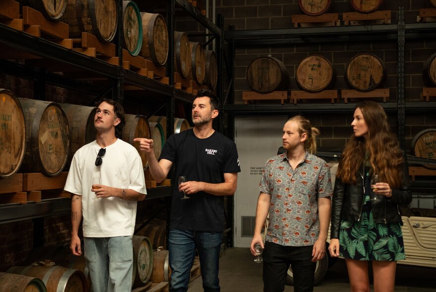 People standing in a barrel-lined cellar, listening to a tour guide.