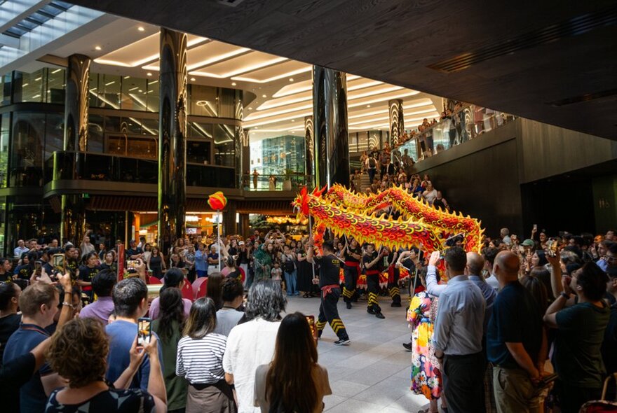Dragon dance performer surrounded by onlookers applauding in an indoor space.