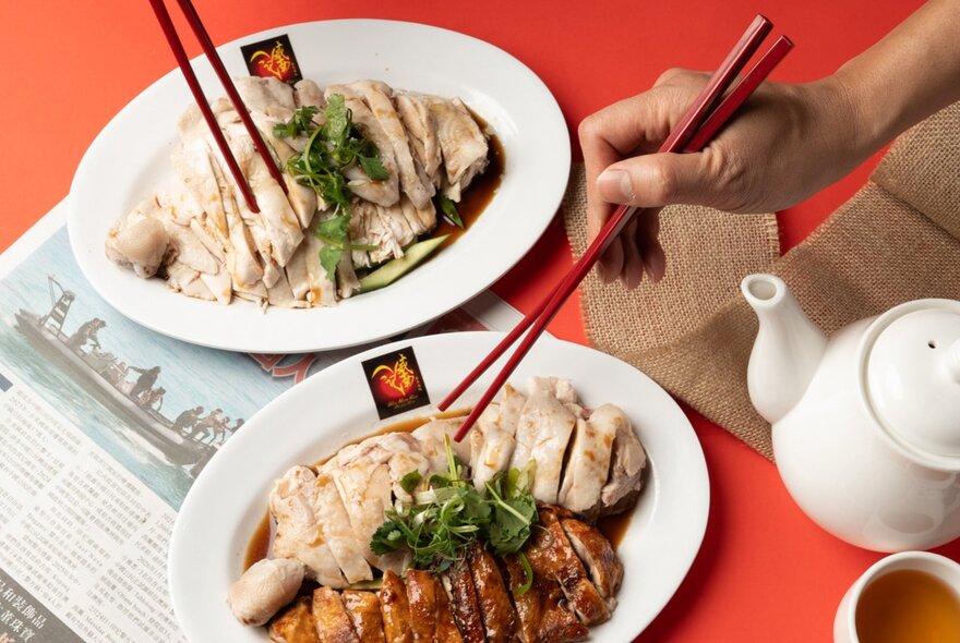 Two dishes of Singaporean chicken with a hand holding chopsticks.