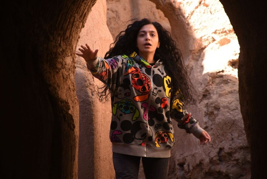 A young woman in a stone doorway of a monument with her hand raised. 