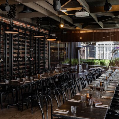 Interior of Soho Restaurant & Bar with two long rows of tables and chairs, a wall of wine bottle and floor to ceiling windows at the rear.