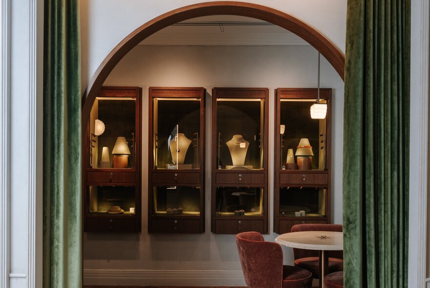 The arched interior of a jewellery store with glass and timber display cases and green velvet curtains.