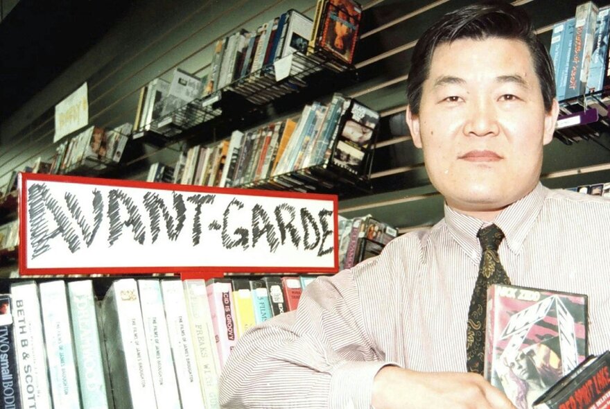 Still from the film Kim's Video, showing the proprietor of Kim's Video store standing in his store in front of shelves of videos.
