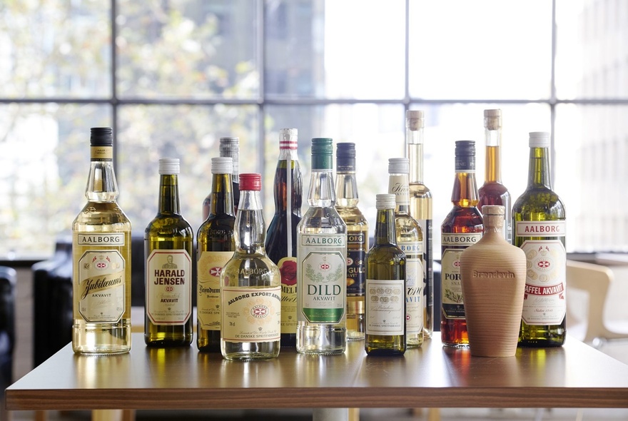 A collection of liquor bottles on a table top near a large window. 
