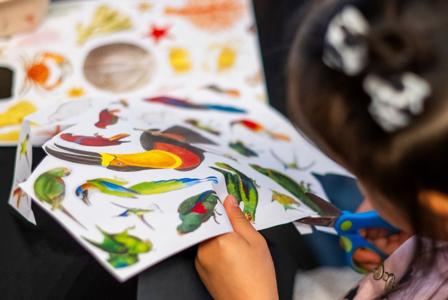 A tight shot of the hands of a child cutting out pictures from paper sheets.