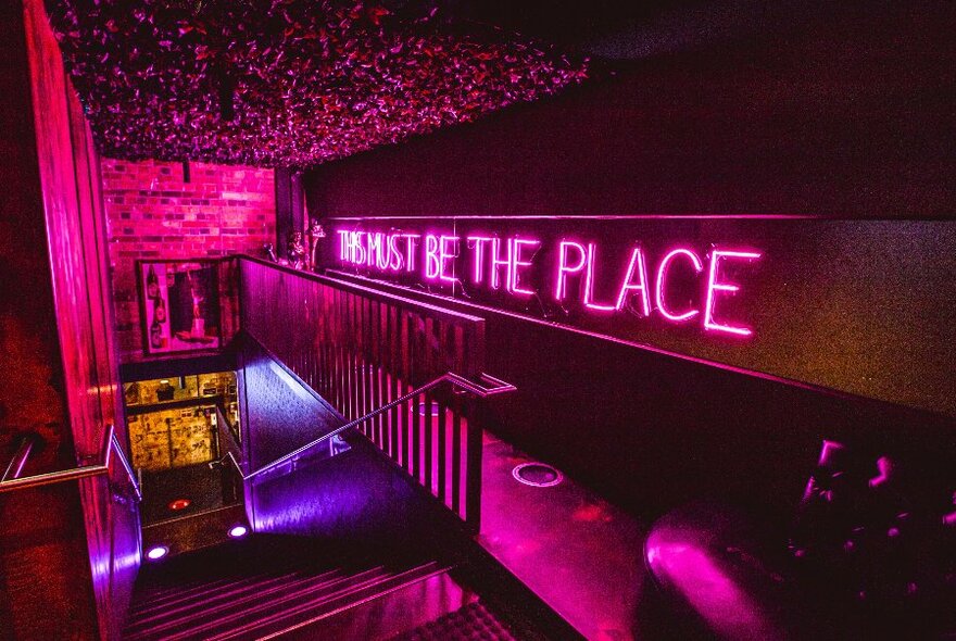 Stairwell, lit pink, pink neon sign on wall to right.