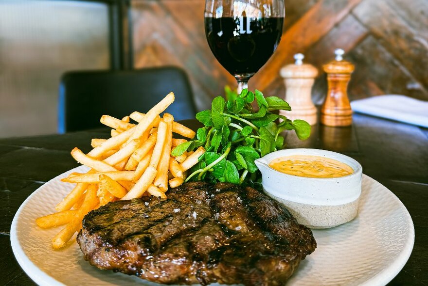 A plate of pub fare, steak and chips with tartare sauce, on a table with a glass of red wine.