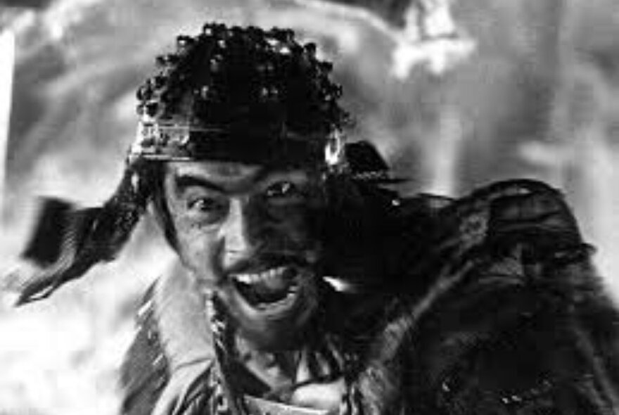 A still from the movie Seven Samurai, of a warrior with his mouth open as if yelling; black and white image..