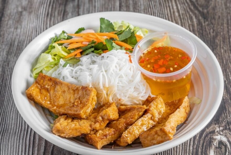 A plate of fried tofu or tempeh, rice noodles, salad and dipping sauce.