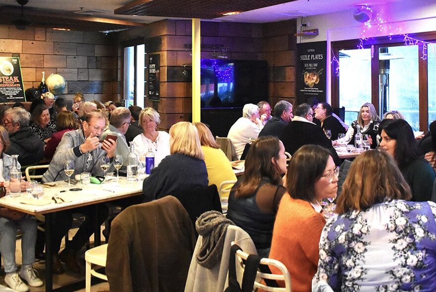 A full dining room with people eating and socialising. 