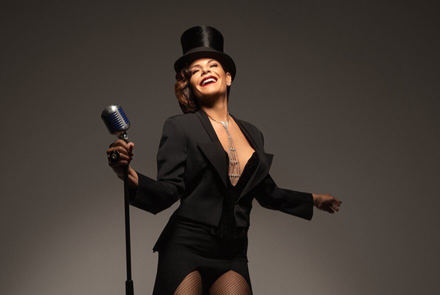 The Countess performer, wearing top hat and revealing tuxedo jacket, holding a retro microphone.