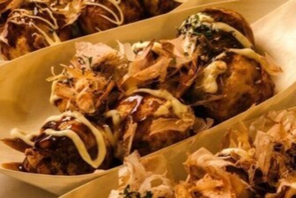 Boat shaped plates of Japanese food drizzled with Kewpie mayo.