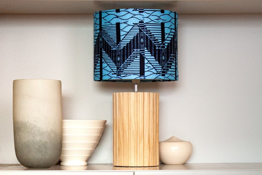 A blue lampshade made using African textiles, on a shelf beside some pottery vessels. 