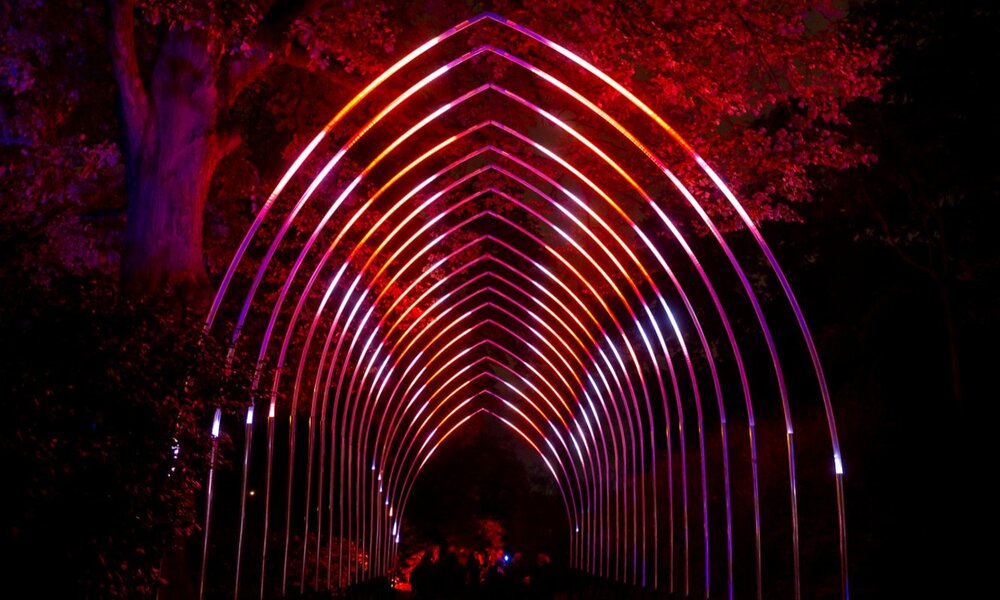 A glowing archway of red lights in a garden at night.