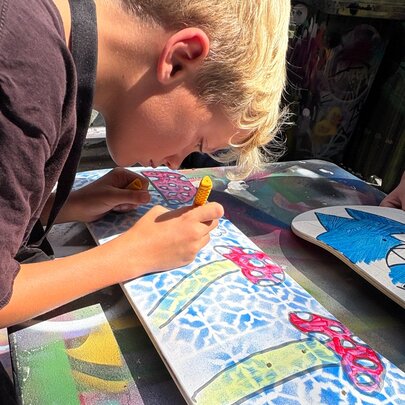 Child adding details to artwork on the back of a skateboard deck.