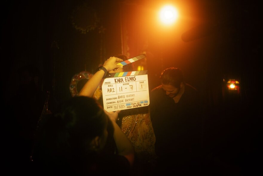 A hand holding a film's clapper board in a night time scene.
