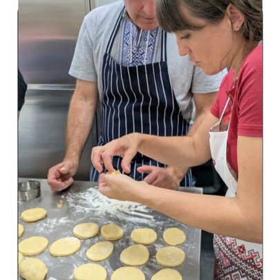 Two people wearing aprons in a commercial kitchen preparing pastry discs.
