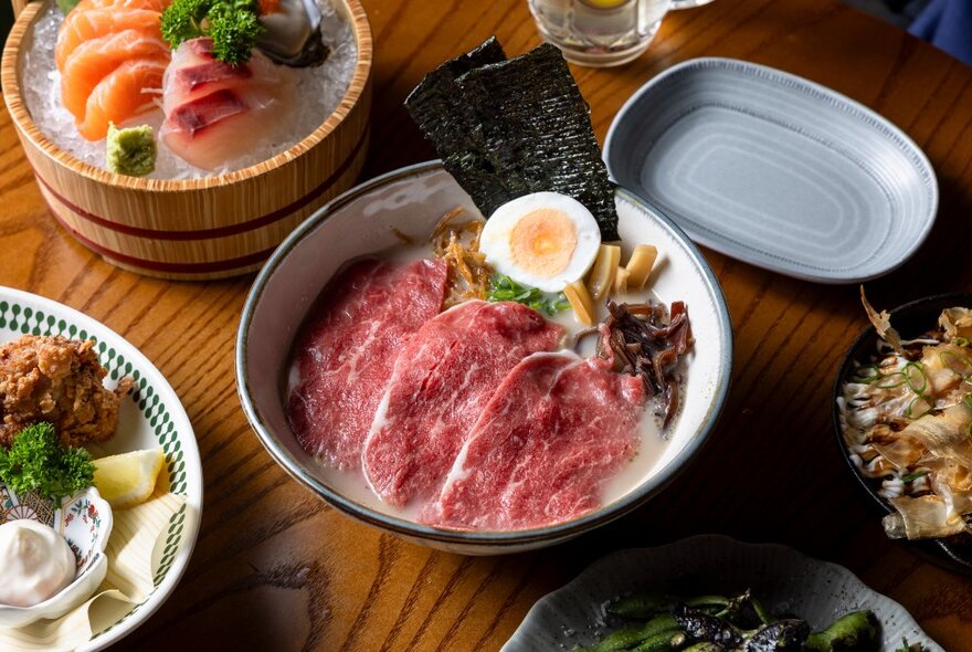 A selection of Japanese dishes presented on a wooden table, including a rare beef dish with half an hard-boiled egg.