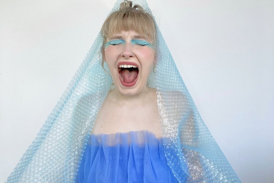 A girl with blue eyeshadow and blue veil, her mouth wide open and eyes closed.