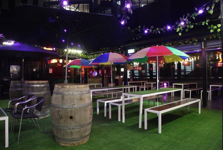 Rooftop bar at night with colourful umbrellas and large barrels. 