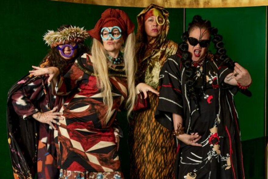 Four women dressed in costumes of earthy hues and using bark, twine and other natural fibres, posing for the camera.