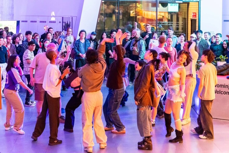 Young people dancing in a large venue while others look on.