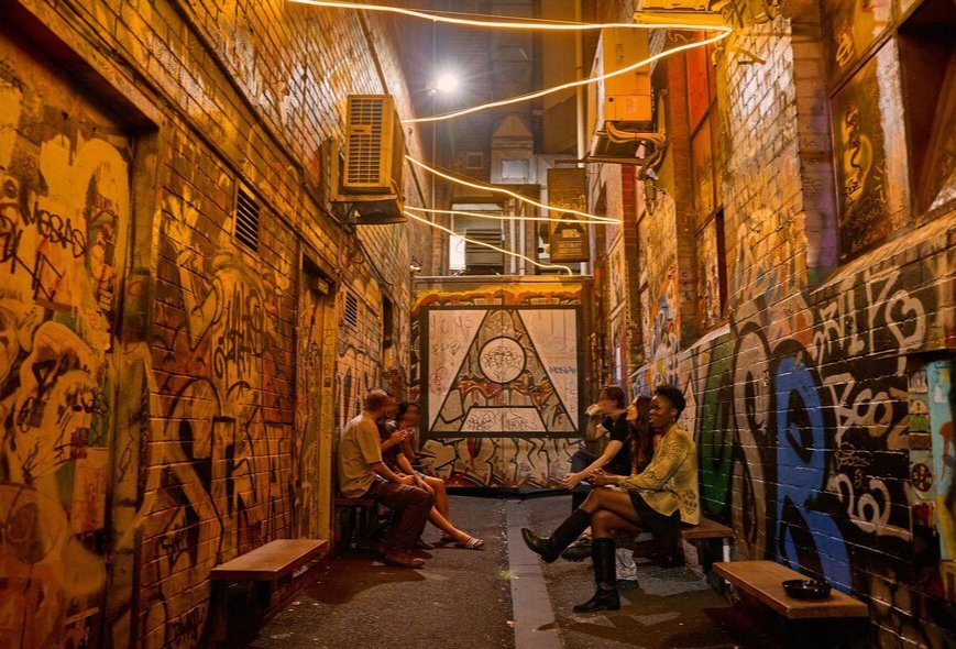 A group of friends are gathered outside a bar in a graffiti-covered laneway