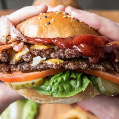 A double cheeseburger literally bursting with ingredients, being held by two hands.