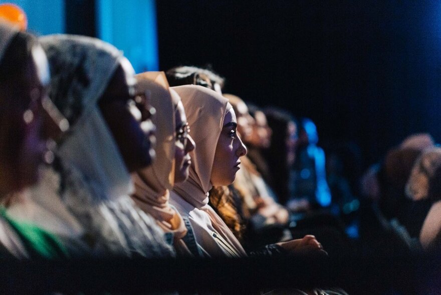 Muslim women seated in an audience row, seen from the side.