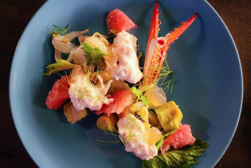 Lobster claw artfully arranged with other food in a shallow blue dish.